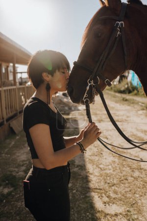 Photo for Young woman with closed eyes kissing horse while spending time on ranch on sunny day - Royalty Free Image