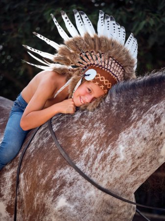 Téléchargez les photos : Jeune garçon portant des coiffures traditionnelles regardant la caméra tout en étant assis et étreignant le cheval avec les rênes - en image libre de droit