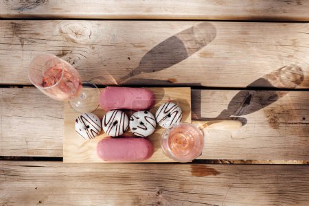Foto de Vasos con vino rosa fino colocados en la superficie de madera cerca del conjunto de deliciosas rosquillas frescas - Imagen libre de derechos