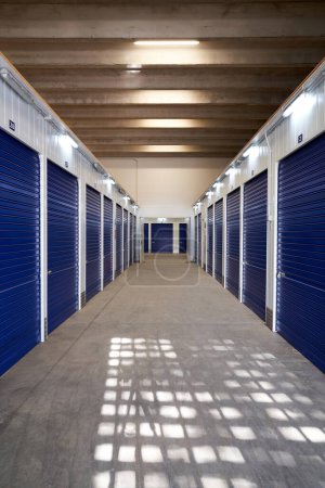 Téléchargez les photos : Long couloir étroit avec rangement avec volets bleus portes automatiques dans un bâtiment industriel pour la location aux entrepreneurs ou aux particuliers - en image libre de droit