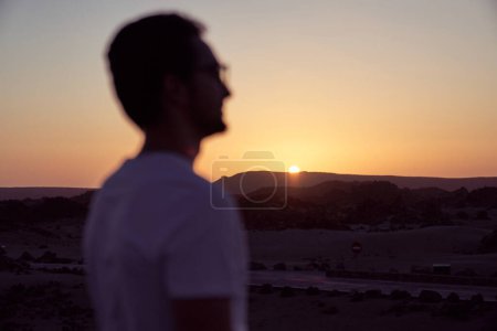 Téléchargez les photos : Vue latérale du voyageur masculin flou admirant le ciel sans nuages au coucher du soleil sur la crête de la montagne pendant le voyage en soirée d'été dans la nature - en image libre de droit