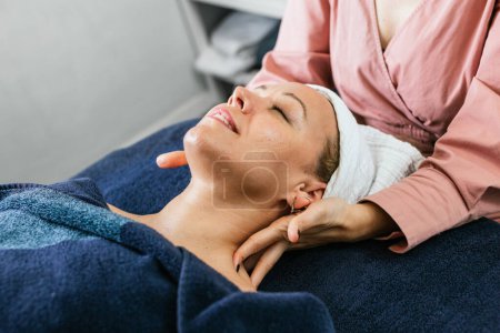 Téléchargez les photos : Recadrée masseuse méconnaissable massant les épaules d'une cliente allongée sur la table dans un salon de beauté - en image libre de droit