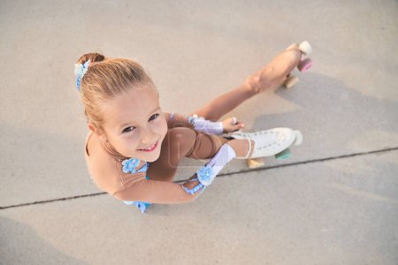 Photo for From above full body of adorable girl in sportswear looking at camera with smile while putting on quad roller skate in city - Royalty Free Image