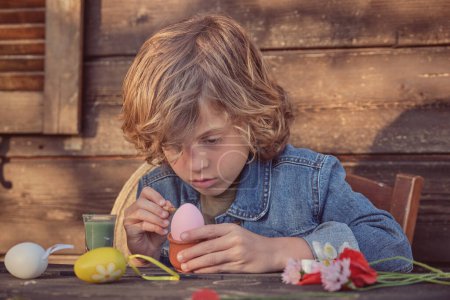 Photo for Cute little kid painting eggs for Easter at table while spending time at home - Royalty Free Image