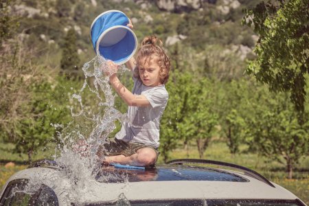Photo for Full length of little kid pouring bucket of water on car in sunny summer day - Royalty Free Image