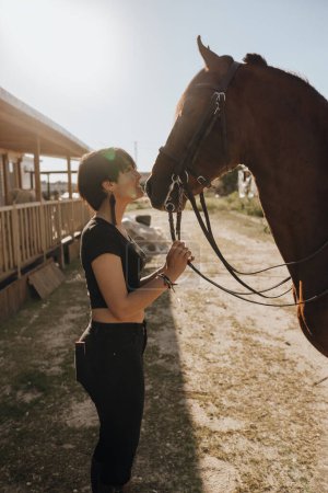 Foto de Mujer joven con los ojos cerrados besando caballo mientras pasa tiempo en el rancho en el día soleado - Imagen libre de derechos