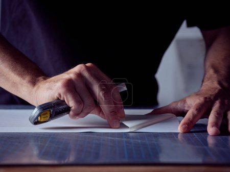 Téléchargez les photos : Recadrage d'artisan anonyme tenant un couteau en papier et retirant l'enveloppe du papier protecteur dans le processus de reliure - en image libre de droit