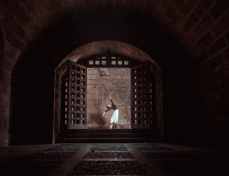 Téléchargez les photos : Vue latérale du corps complet de la danseuse de ballet femme dansant dans le passage sombre de l'ancien bâtiment près du mur de pierre - en image libre de droit