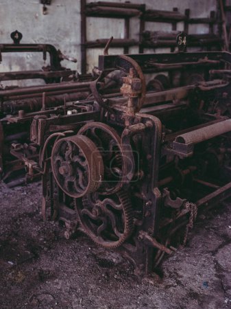 Photo for Aged rusty iron loom with gears and mechanism placed near shabby stone wall in abandoned industrial yarn factory - Royalty Free Image