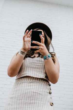 Foto de Mujer atractiva de pelo largo irreconocible en la mensajería de sombrero en el teléfono móvil - Imagen libre de derechos