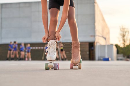 Téléchargez les photos : Crop fille méconnaissable tirant leggings sur le patinage à roulettes quad vintage tout en se tenant sur le chemin pendant la préparation de l'entraînement le jour d'été en ville - en image libre de droit