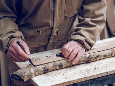 Téléchargez les photos : Cultivez des travailleurs du bois masculins méconnaissables en vêtements de travail en mesurant et en marquant les détails en bois avec un stylo feutre tout en travaillant dans la campagne - en image libre de droit