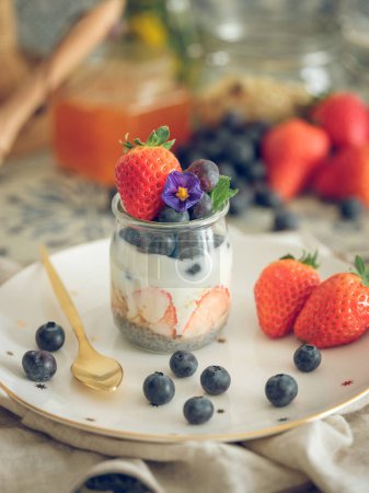 Photo for Appetizing healthy yogurt with fresh strawberries and blueberries in jar placed on table with spoon for healthy breakfast - Royalty Free Image