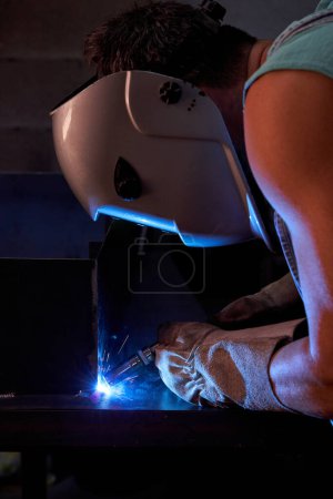 Photo for Side view of unrecognizable male welder in protective helmet welding metal construction while working in professional workshop with dim light - Royalty Free Image