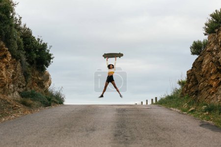Téléchargez les photos : Saut ethnique féminin avec longboard sur route asphaltée - en image libre de droit