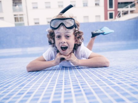 Foto de Desde abajo de niño preadolescente alegre en máscara de snorkel y aletas acostado en fondo de baldosas azules de la piscina vacía y mirando a la cámara - Imagen libre de derechos