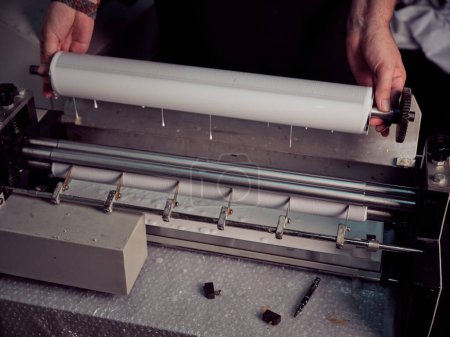 Photo for From above of crop anonymous male bookbinder putting roller with glue into machine while working at workbench in professional workshop - Royalty Free Image