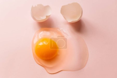 Photo for From above raw broken egg with yellow yolk and eggshells on pink background - Royalty Free Image