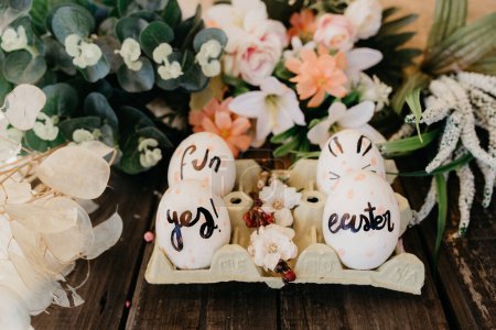 Foto de Conjunto de huevos de gallina de colores en recipiente entre flores ornamentales sobre fondo de madera - Imagen libre de derechos