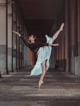 Téléchargez les photos : Corps complet de ballerine gracieuse en jupe de soie et chaussures pointes équilibrage en position de ballet arabesque dans le passage vide du bâtiment - en image libre de droit