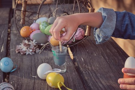 Photo for Crop child painting eggs for Easter at wooden table on sunny summer day - Royalty Free Image