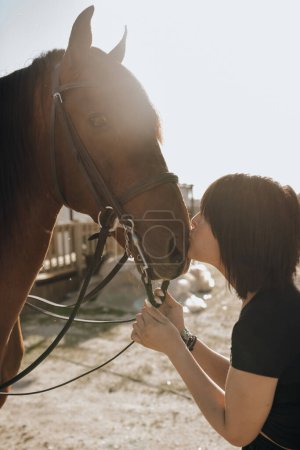 Foto de Mujer joven con los ojos cerrados besando caballo mientras pasa tiempo en el rancho en el día soleado - Imagen libre de derechos