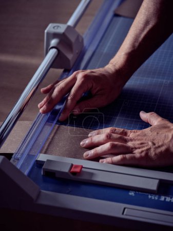Foto de Alto ángulo de artesano masculino anónimo utilizando la máquina de corte y trabajando con papel en el banco de trabajo en el taller de encuadernación - Imagen libre de derechos