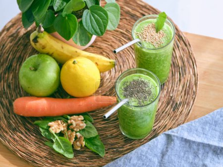 Photo for From above glasses of green smoothies with seeds on rattan mat with various fruits and carrot near potted basil plant - Royalty Free Image