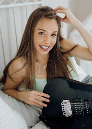 Téléchargez les photos : D'en haut Jeune femme brune jouant de la guitare sur le lit - en image libre de droit