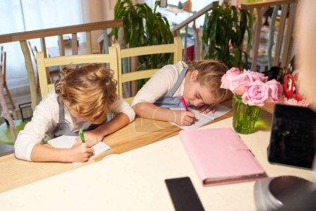 Foto de Desde arriba de alumnos rubios diligentes tomando notas en copybooks mientras están sentados juntos en la mesa - Imagen libre de derechos