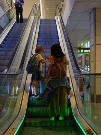 Foto de Vista trasera de la mujer y el niño con el equipaje a la espera de la salida en la terminal del aeropuerto y el hombre de la cosecha bajando escaleras mecánicas - Imagen libre de derechos