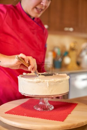 Téléchargez les photos : Recadrer gâteau de décoration confiseur femelle avec crème au beurre à l'aide de spatule et debout au comptoir de la cuisine - en image libre de droit