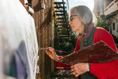 Foto de Desde abajo vista lateral de artistas femeninas envejecidas pintando sobre lienzo en el patio trasero en el día soleado en verano - Imagen libre de derechos