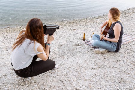 Foto de Mujer joven disparando amigo tocando la guitarra - Imagen libre de derechos
