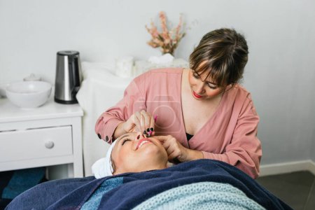 Téléchargez les photos : Femme cosmétologue arrachant les sourcils sur le visage de la cliente allongée sur la table dans un salon de beauté - en image libre de droit