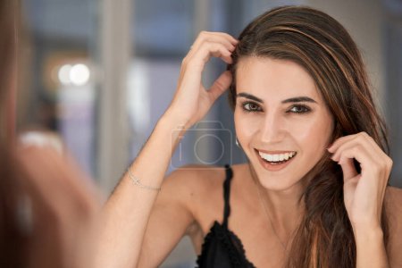 Photo for Cheerful female client touching hair and looking at camera with smile through mirror while standing in modern light beauty salon - Royalty Free Image