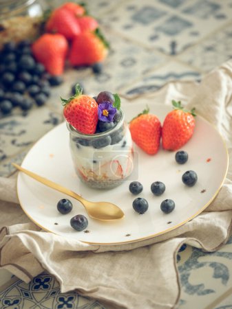 Photo for High angle of sweet tasty yogurt in jar served with ripe strawberries and blueberries for breakfast in morning at home - Royalty Free Image
