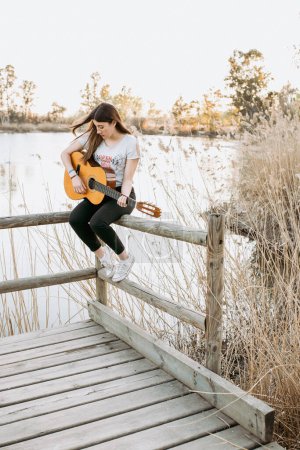 Téléchargez les photos : Jeune femme jouant de la guitare près de l'eau - en image libre de droit