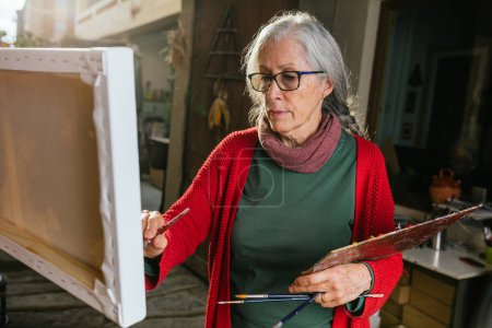 Téléchargez les photos : Artistes féminines âgées peignant sur toile dans la cour par une journée ensoleillée en été - en image libre de droit