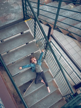 Foto de Desde arriba de cuerpo completo preadolescente niño acostado en las escaleras de la escalera con monopatín y gritando en voz alta - Imagen libre de derechos