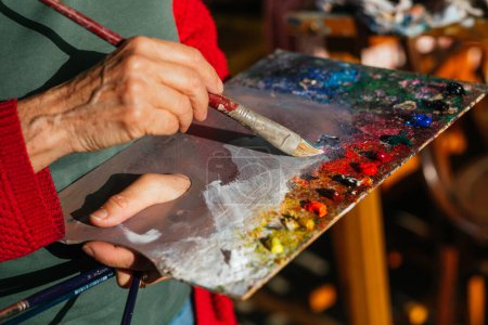 Photo for From above of crop unrecognizable senior female painter mixing colors on paint palette in art workshop - Royalty Free Image