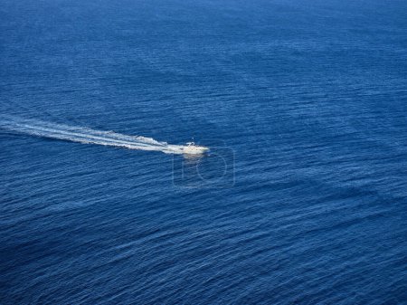 Foto de Vista de ángulo alto del barco blanco flotando en agua de mar ondulada azul y dejando rastro espumoso detrás - Imagen libre de derechos