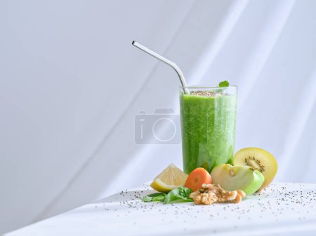 Foto de Refrescante batido verde servido en la mesa con frutas frescas cortadas y zanahoria con nuez sobre fondo blanco en estudio de luz - Imagen libre de derechos
