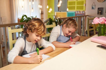 Foto de Niño y niña preadolescentes mirando hacia abajo mientras realizan ejercicios de escritura en copybooks juntos en la lección - Imagen libre de derechos