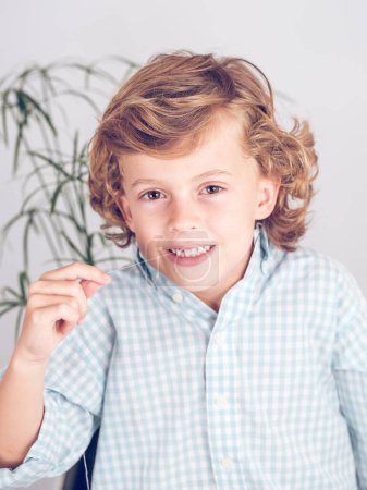 Foto de Adorable niño preadolescente valiente con el pelo rizado sacudiendo los dientes con hilo y mirando a la cámara - Imagen libre de derechos
