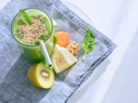 Téléchargez les photos : Du dessus verre de boisson de désintoxication verte avec des graines de sésame servi sur assiette avec divers fruits et carotte sur fond blanc - en image libre de droit