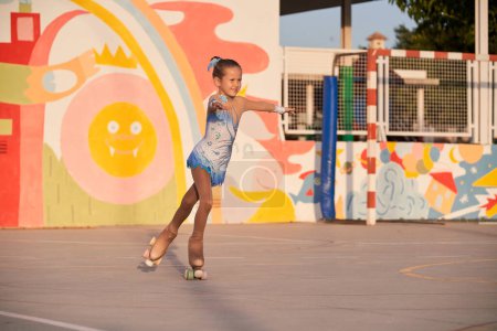 Téléchargez les photos : Corps complet de talentueuse fille énergique en justaucorps chevauchant des patins à roulettes quad pendant l'entraînement sur un terrain de sport lors d'une journée d'été ensoleillée - en image libre de droit