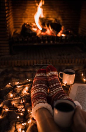 Photo for Faceless woman sitting by fireplace and holding mug - Royalty Free Image