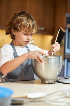 Foto vertical de un niño mezclando ingredientes en un recipiente metálico