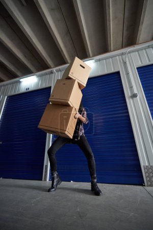 Foto de Persona irreconocible con montón de cajas de cartón que caen embaladas con pertenencias en las manos de pie cerca de auto almacenamiento cerrado durante el día en movimiento - Imagen libre de derechos